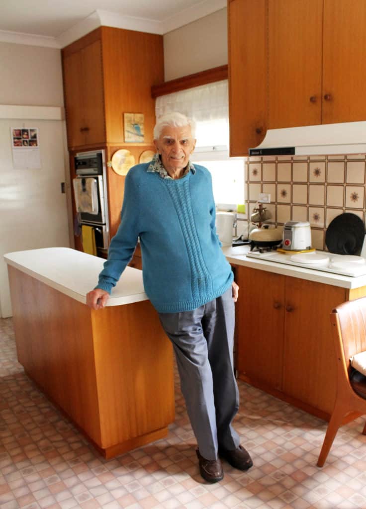 Elderly man leaning against kitchen benchtop 