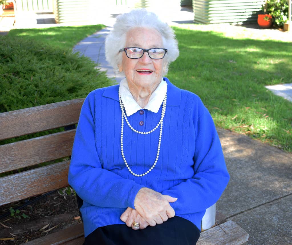 100 year old lady with blue jumper sitting on outdoor bench