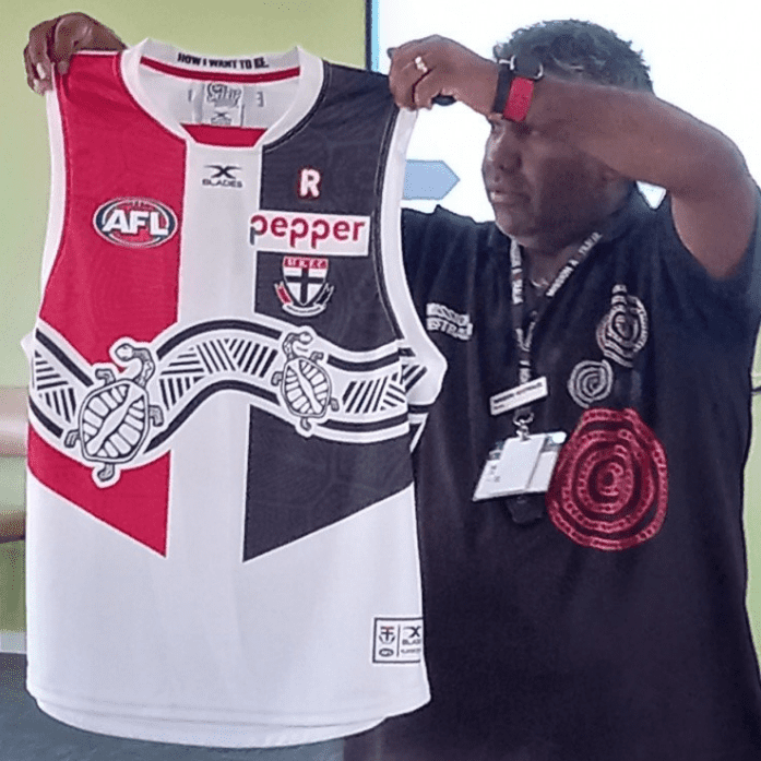 Sam Mitchell from Mission Australia holding a football jersey adorned with Aboriginal