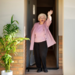 older lady waves at the camers from an open doorway