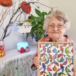 Older lady holding a framed artwork in front of Halloween decorations