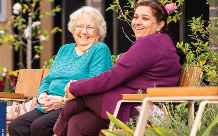 old lady with carer sitting on bench outdoors laughing