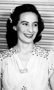 A black and white photograph depicting a young woman in a formal dress, smiling and looking to her left.