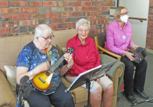 Trio of elderly women singing and playing ukulele and concertina