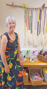 Female volunteer standing in front of all her colourful craftwork and artwork