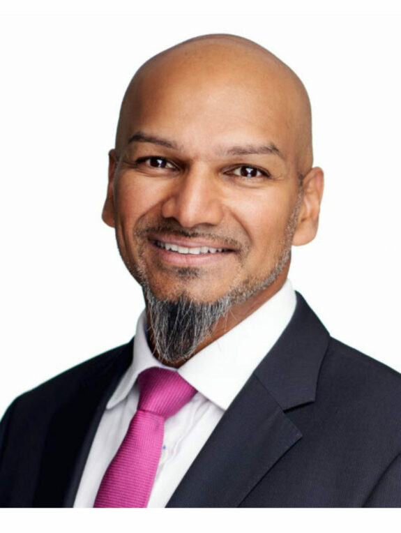 Bald man smiling and wearing a black suit with pink tie